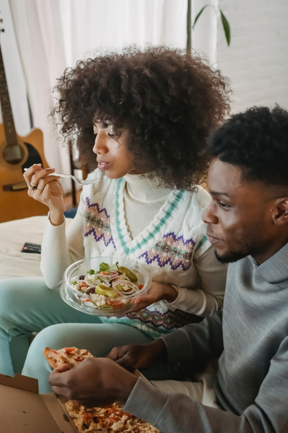 Young black couple resting on couch and eating delivered food during weekend at home